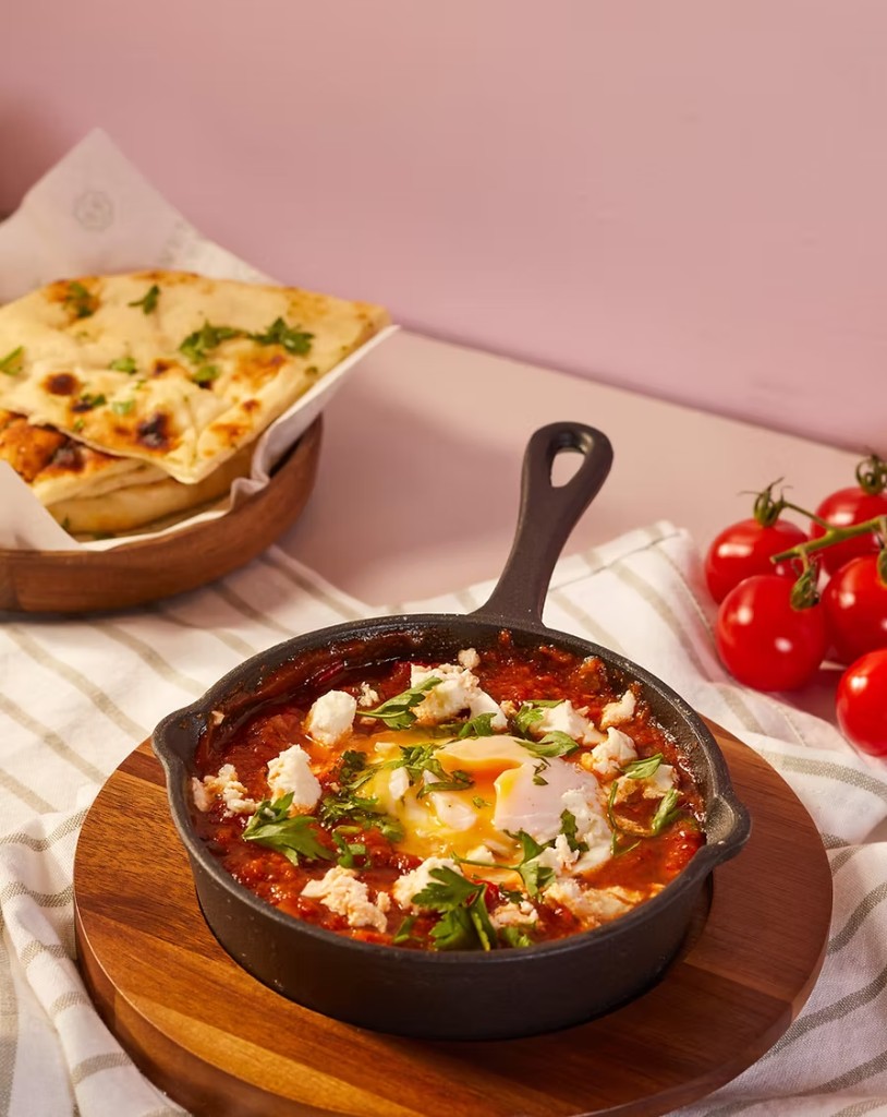 Shakshuka in a cast iron skillet with flatbread and cherry tomatoes