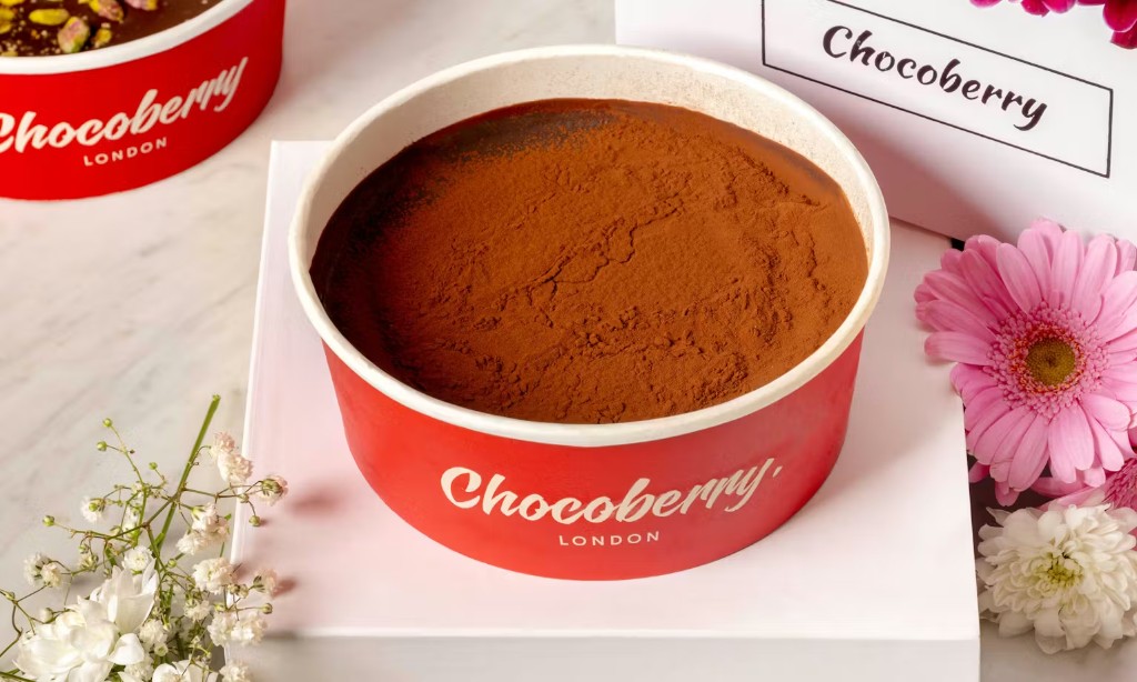 Cocoa-dusted dessert in a red gift tub with flowers on marble