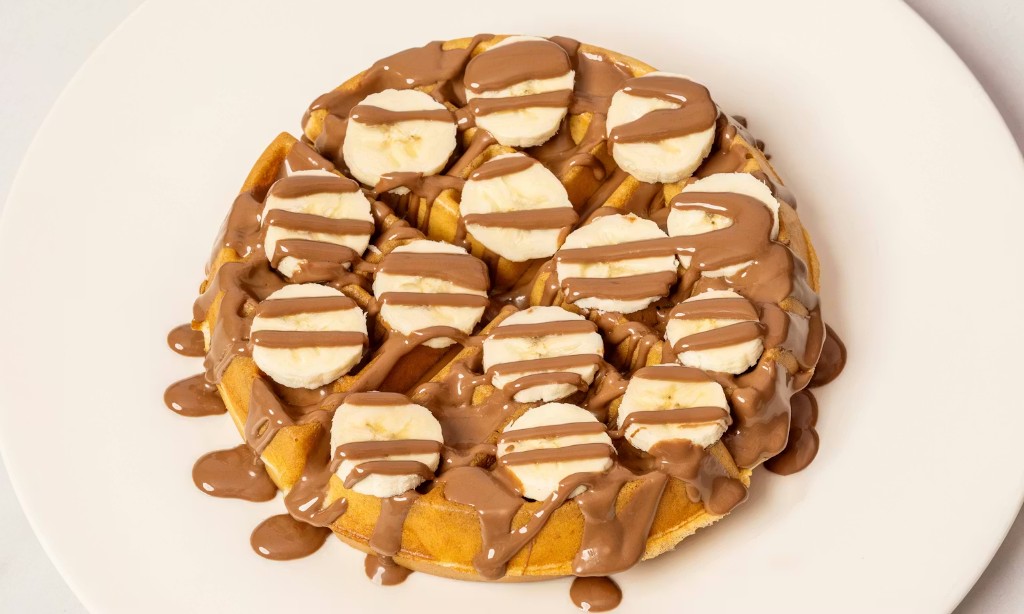 Belgian waffle with banana slices and chocolate sauce on a white plate